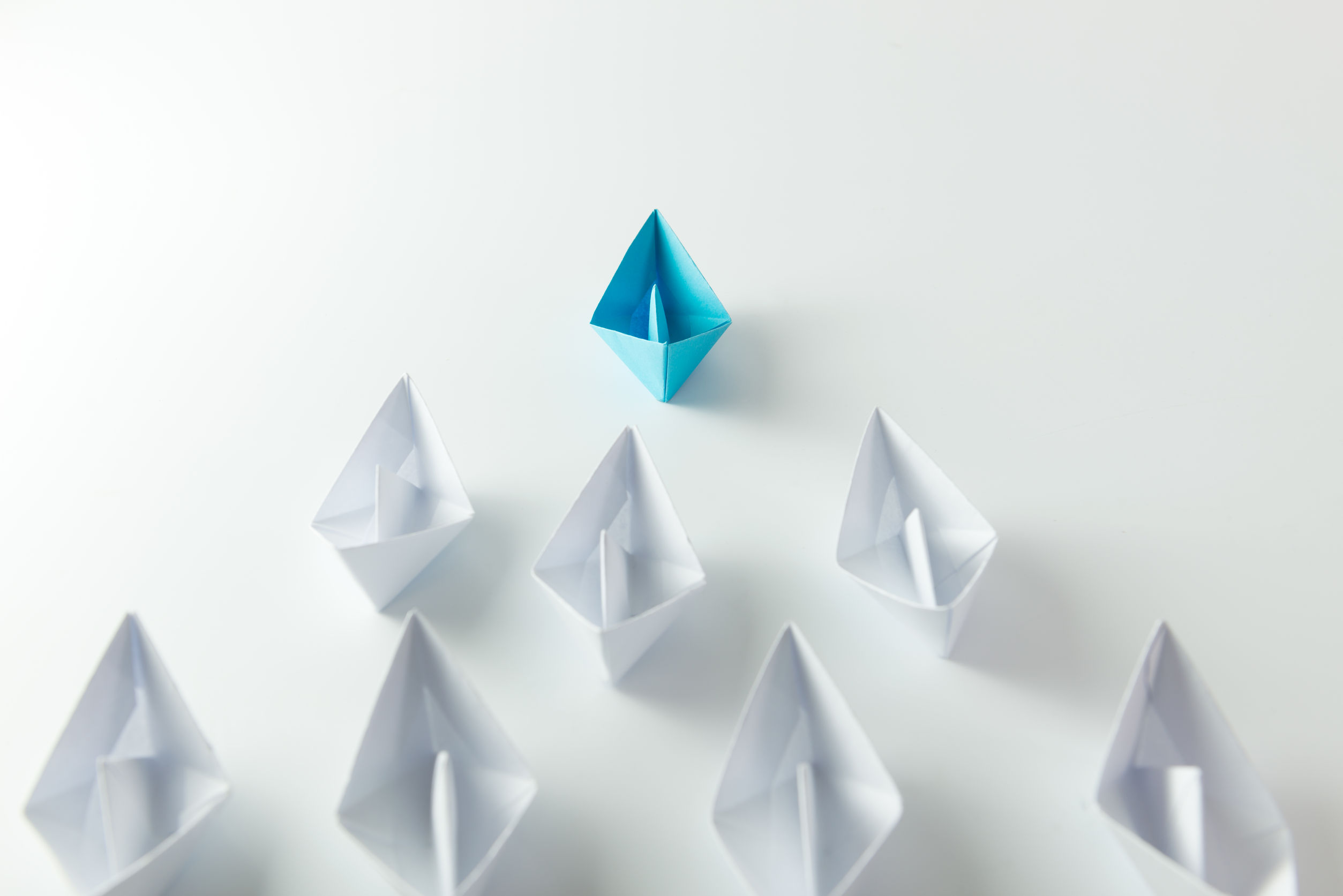 Photo of leadership concept with blue paper ship leading among white