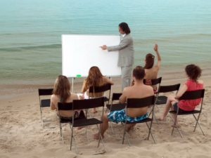 Man in suit teaching class of students on beach for learning strategies concept