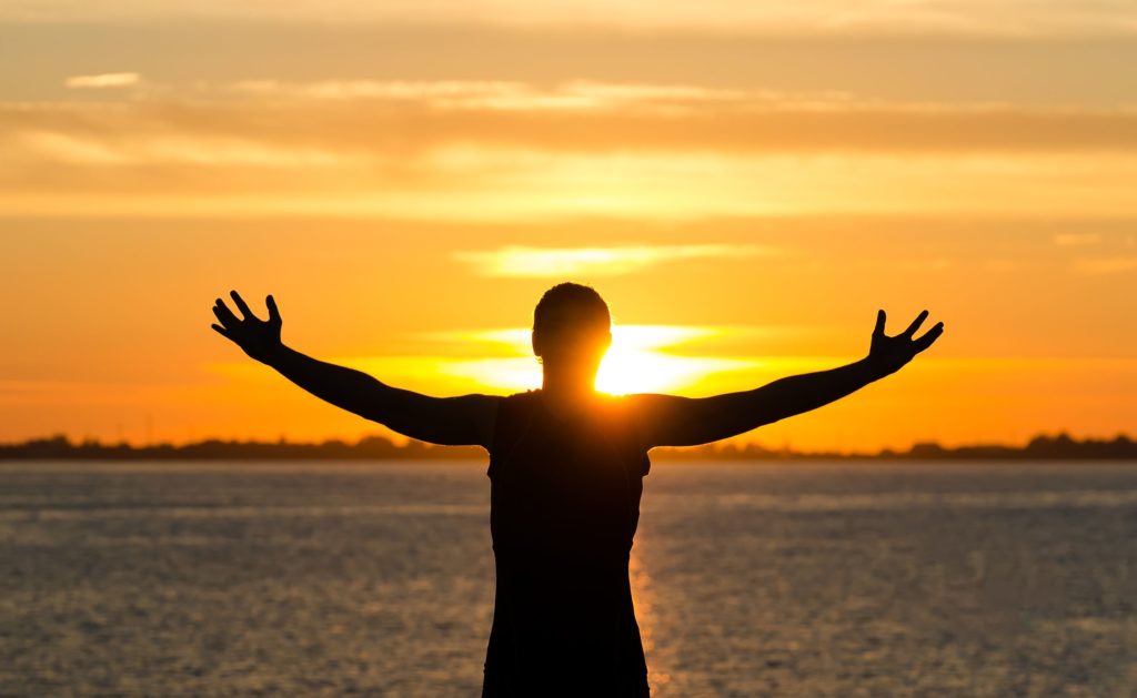 photo of man with arms wide open on the beach at sunrise