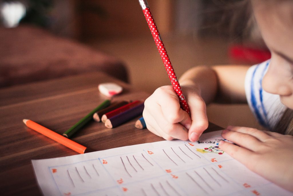 Photo of kid writing with colored pencils