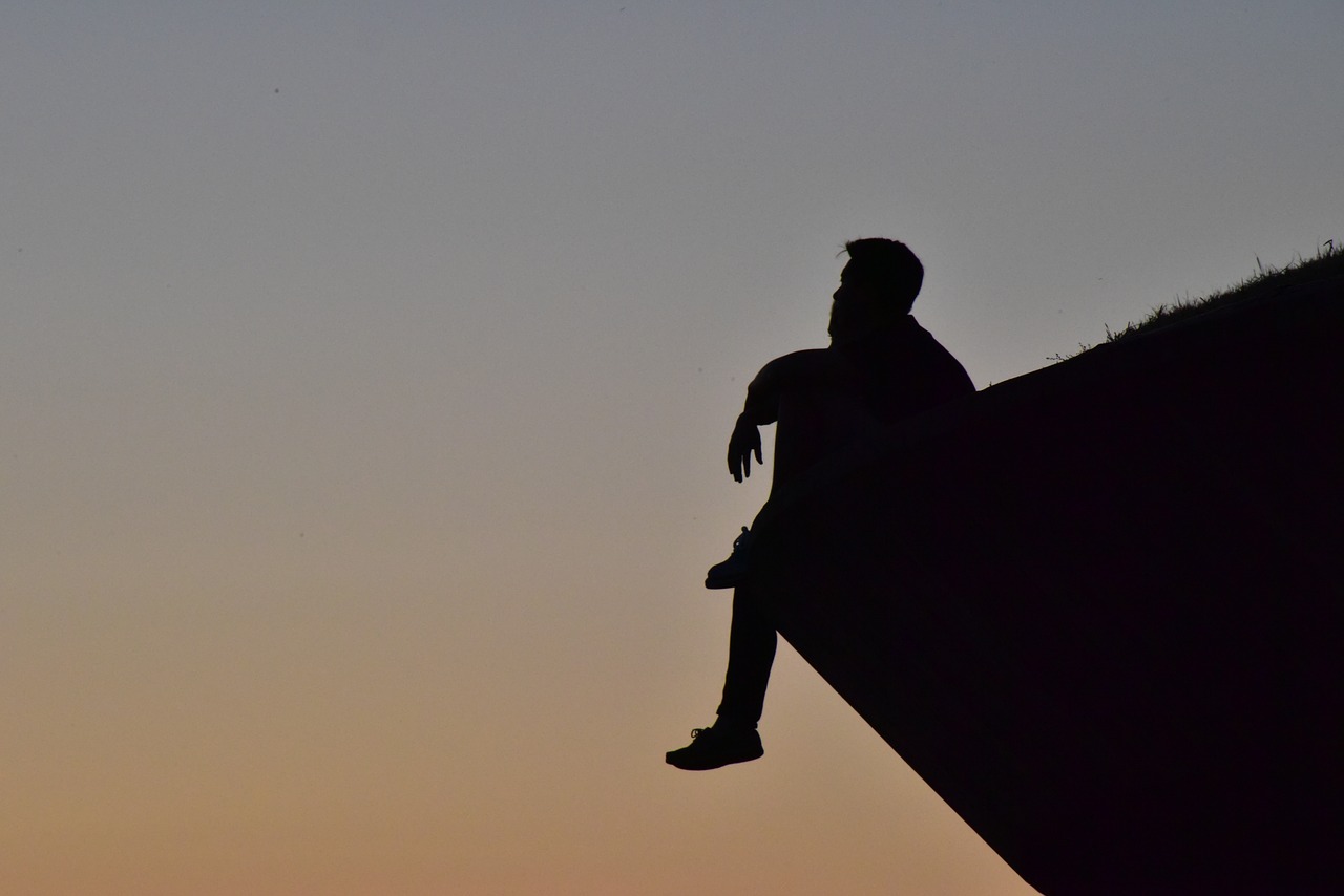Photo of silhouette of reflective man sitting on rock outcropping