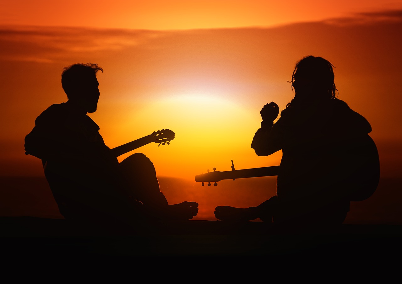 Silhouette of two sitting guitar players against sunset for post on benefits of learning an instrument